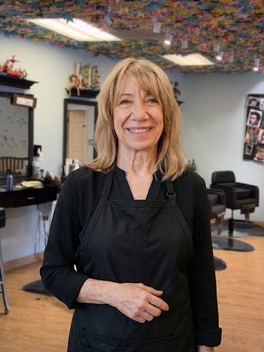 Carol Spears, owner and stylist at Kids Cuts, smiling in the salon beneath the paper-crane ceiling.