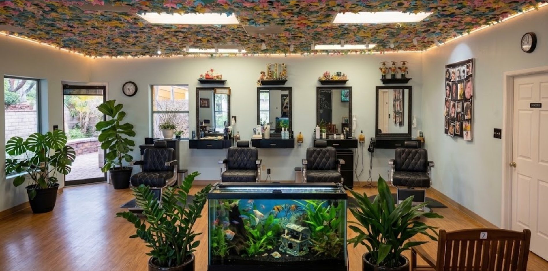 Inside Kids Cuts: four styling chairs facing framed mirrors, a large aquarium in the middle of the room, houseplants, and a ceiling covered in thousands of colorful paper cranes.