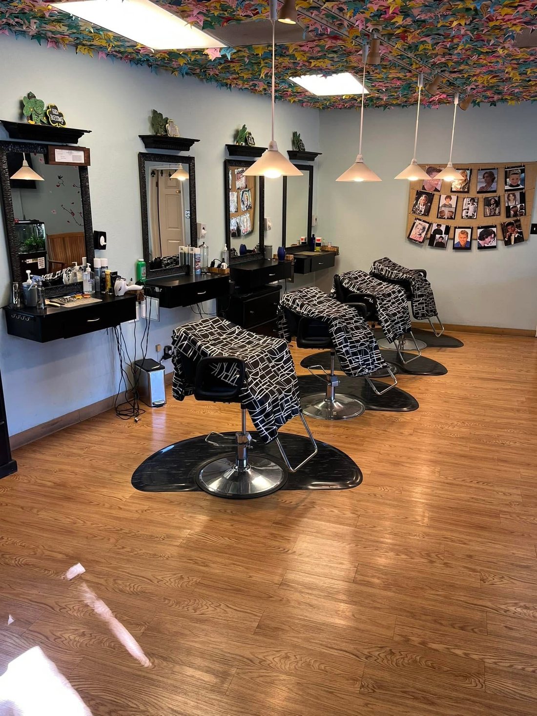 A row of Kids Cuts styling stations with black framed mirrors, pendant lights, patterned capes over the chairs, and a wall of children's haircut photos.